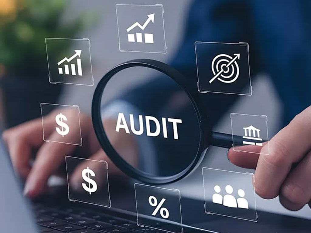 Magnifying glass labeled AUDIT over finance and analytics icons on a laptop